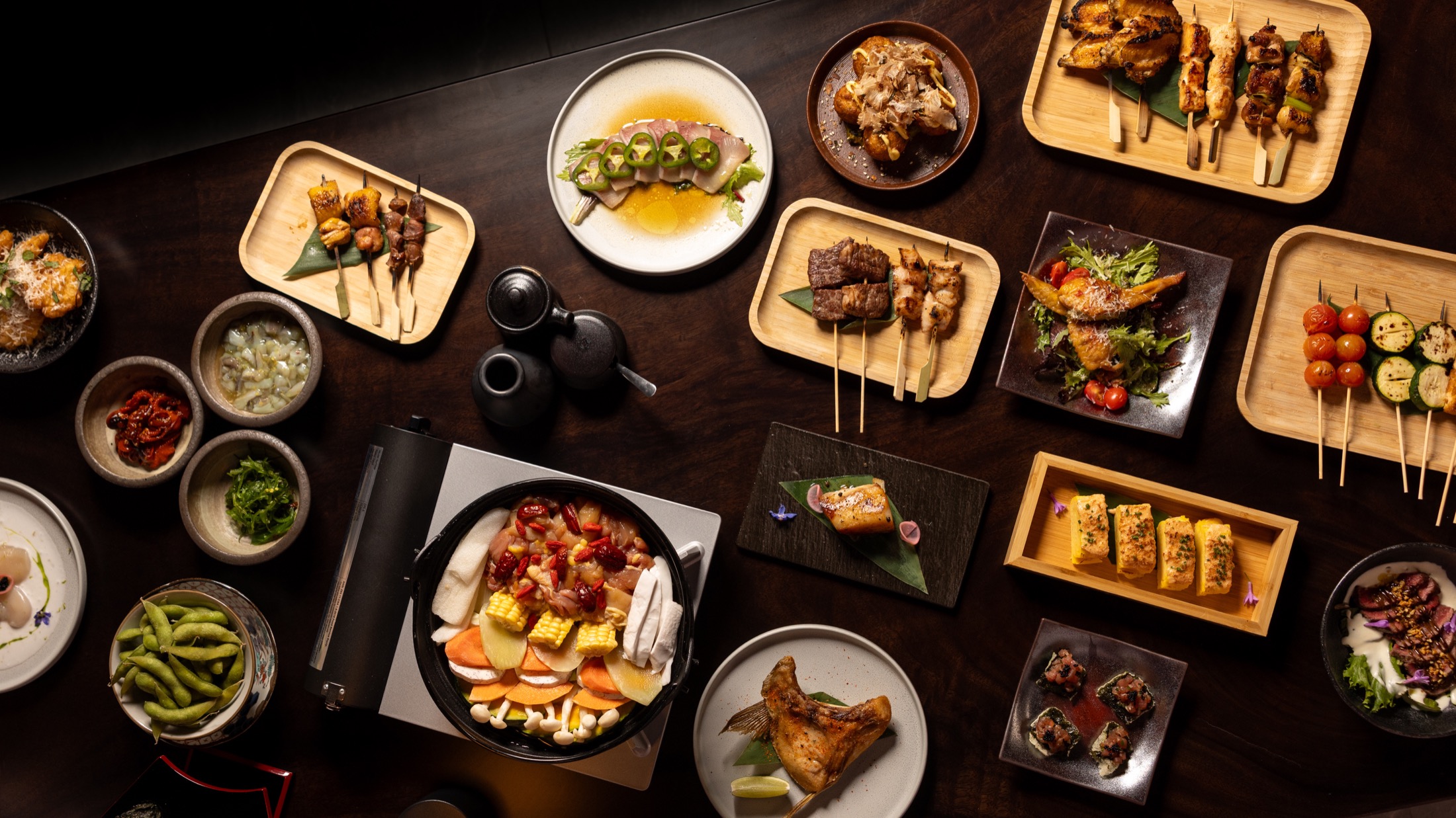 Overhead spread of nabe, yakitori, appetizers, and drinks